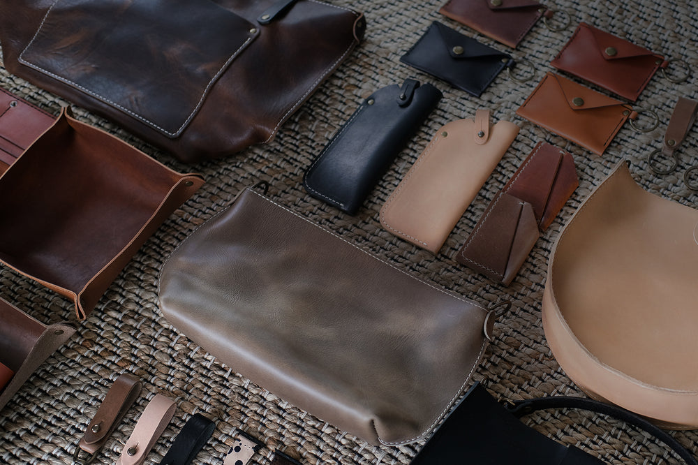 Leather bags, cases, wallets and keychains in various natural colors laid out in a grid pattern